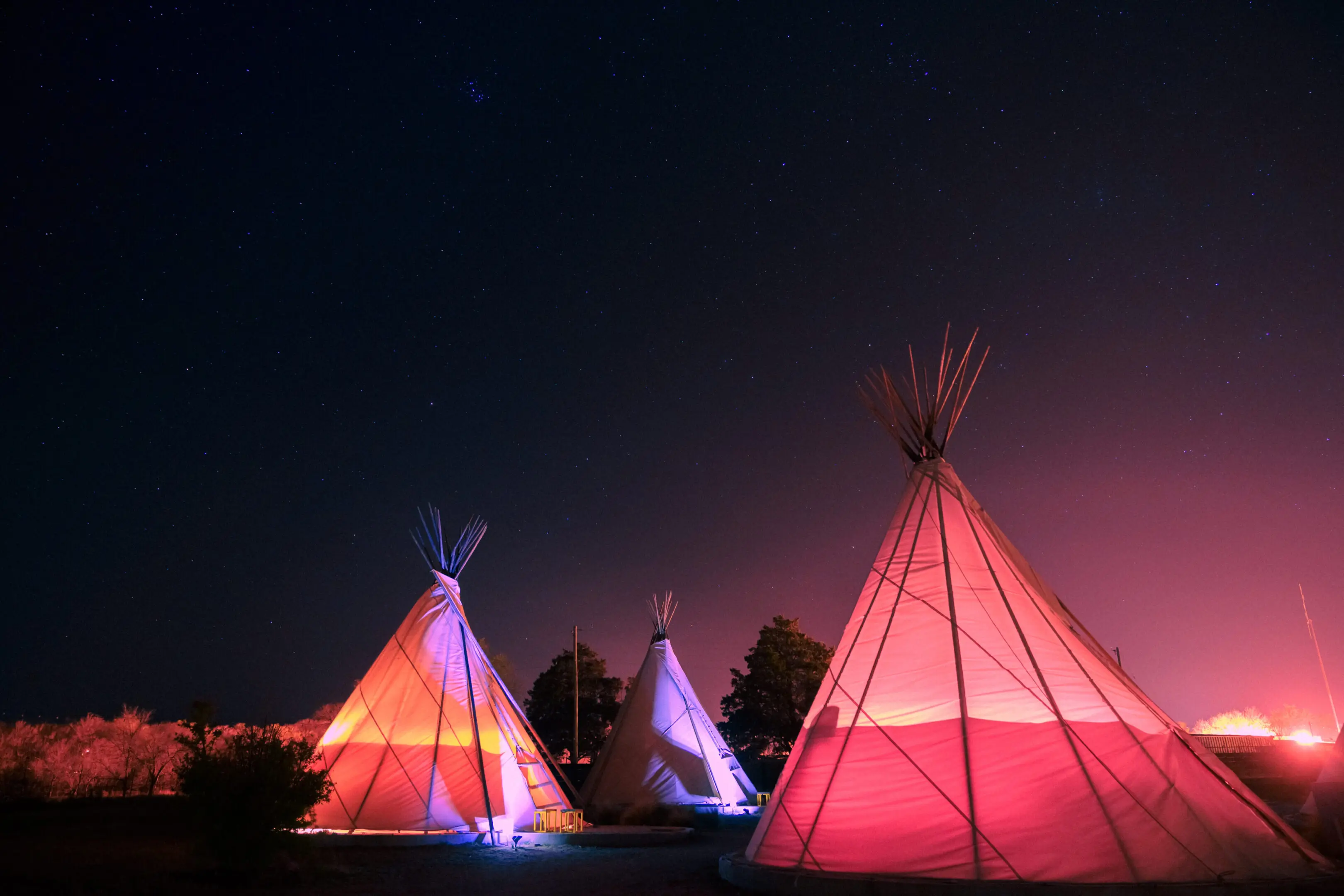 Illuminated teepees glowing under the night sky.