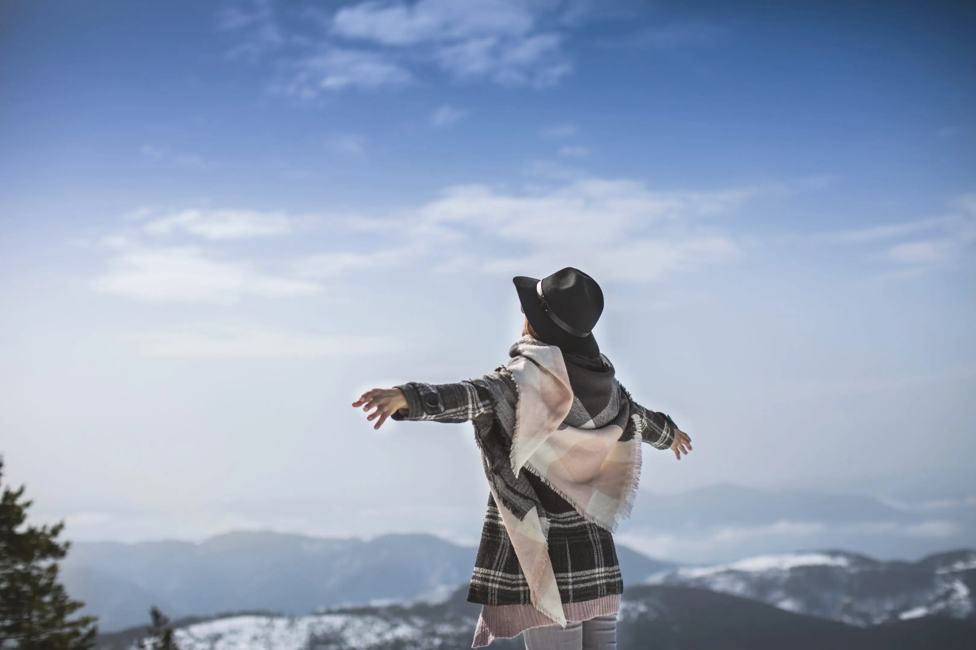 Person joyfully throwing snow in a mountainous winter landscape.