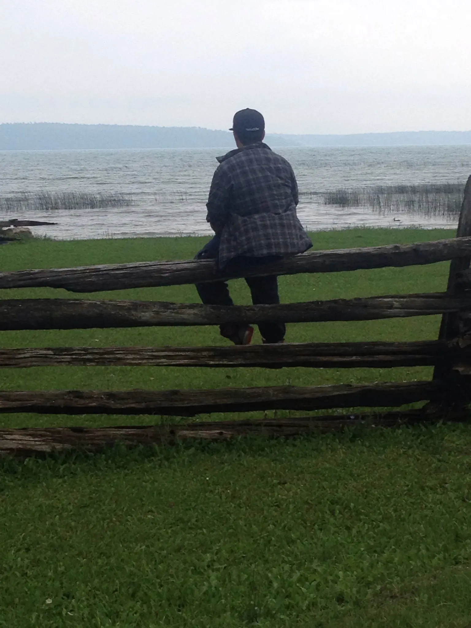 Person sitting on a wooden fence overlooking a calm sea.